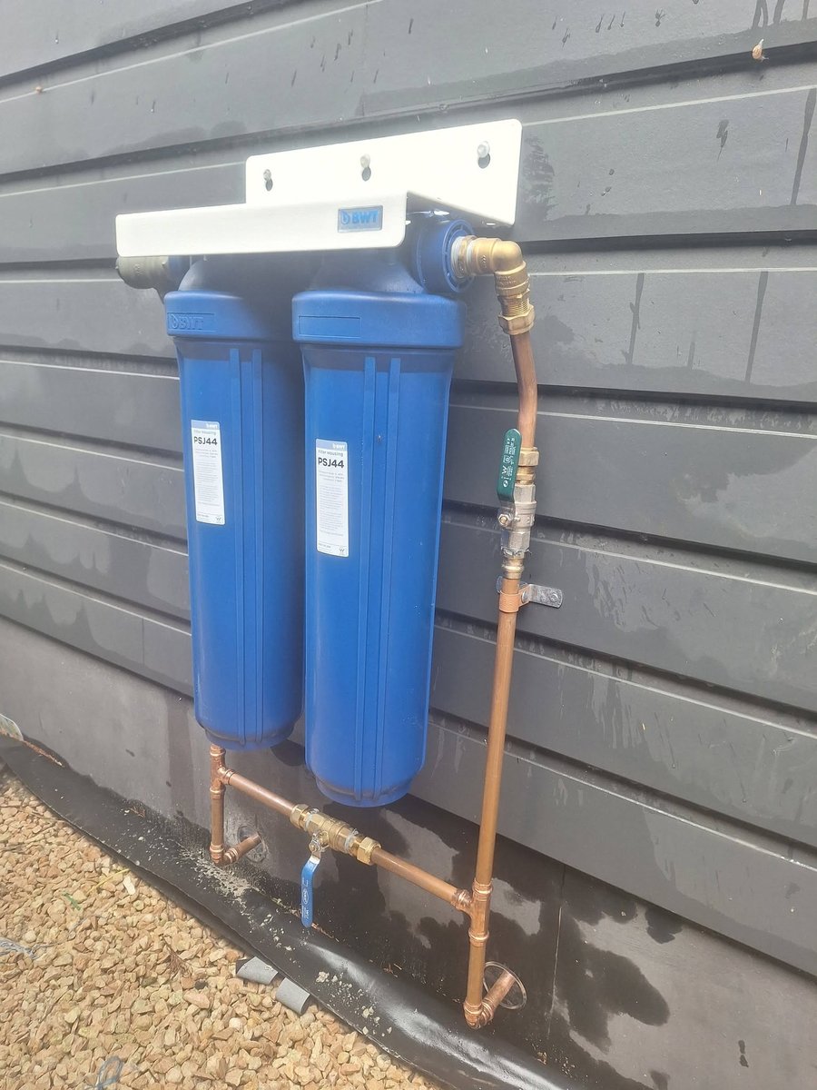 Twin water filter housings plumbed in copper on a weatherboard wall